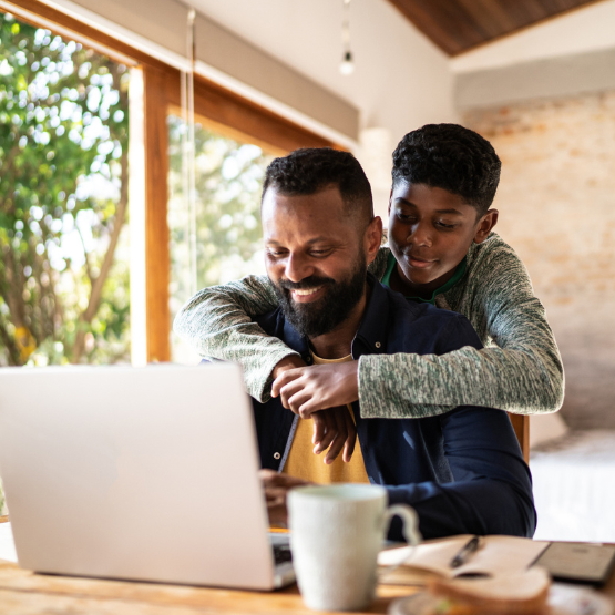 Young son hugging dad working on his computer