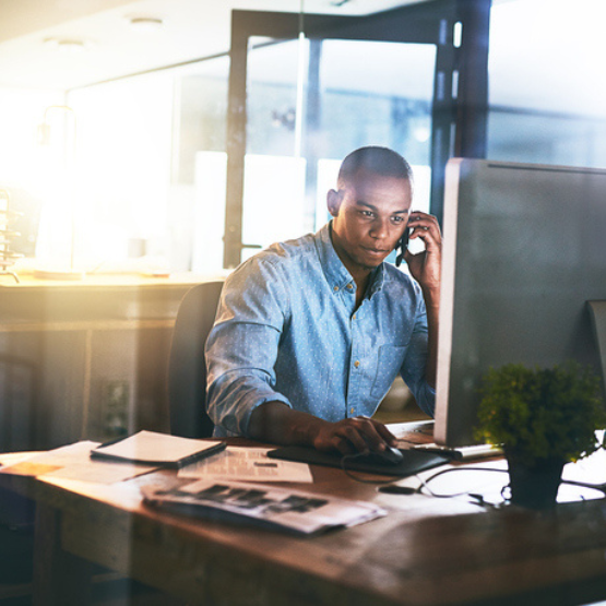 Person sitting at desk talking on phone while looking at computer screen