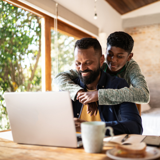 Young son hugging dad working on his computer